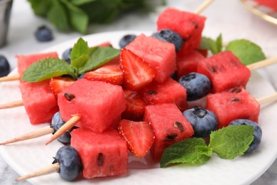 Photo of Skewers with tasty watermelon, strawberries, blueberries and mint on table, closeup