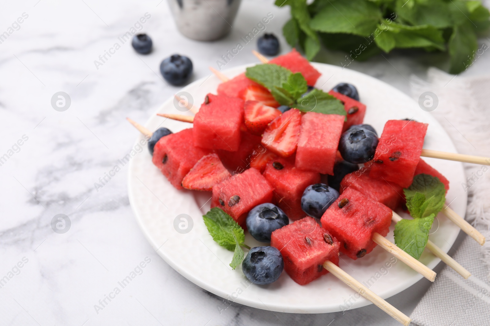 Photo of Skewers with tasty watermelon, strawberries, blueberries and mint on white marble table, closeup