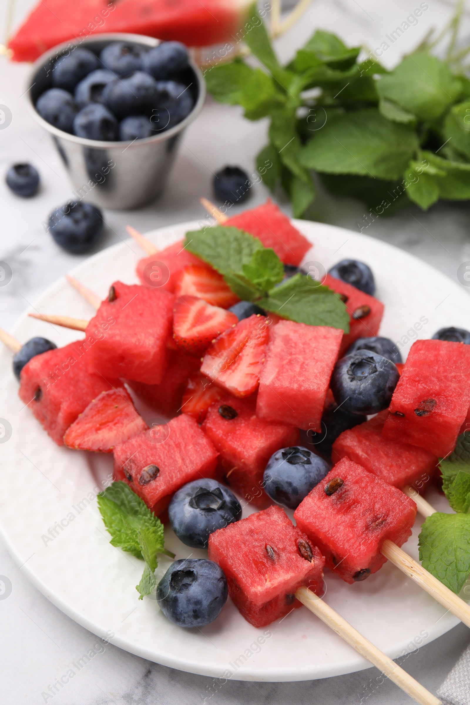 Photo of Skewers with tasty watermelon, strawberries, blueberries and mint on light table, closeup