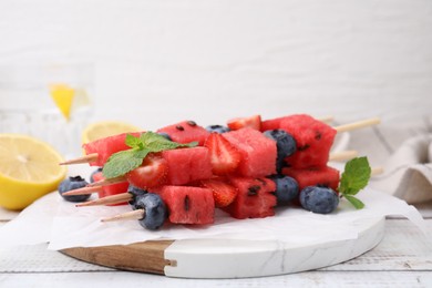 Photo of Skewers with tasty watermelon, strawberries, blueberries and mint on light wooden table, closeup