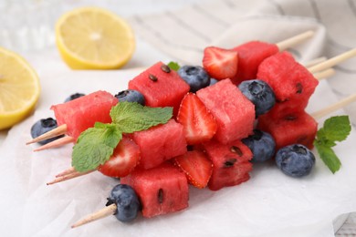 Photo of Skewers with tasty watermelon, strawberries, blueberries and mint on table, closeup