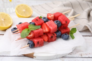 Photo of Skewers with tasty watermelon, strawberries, blueberries and mint on light wooden table, closeup