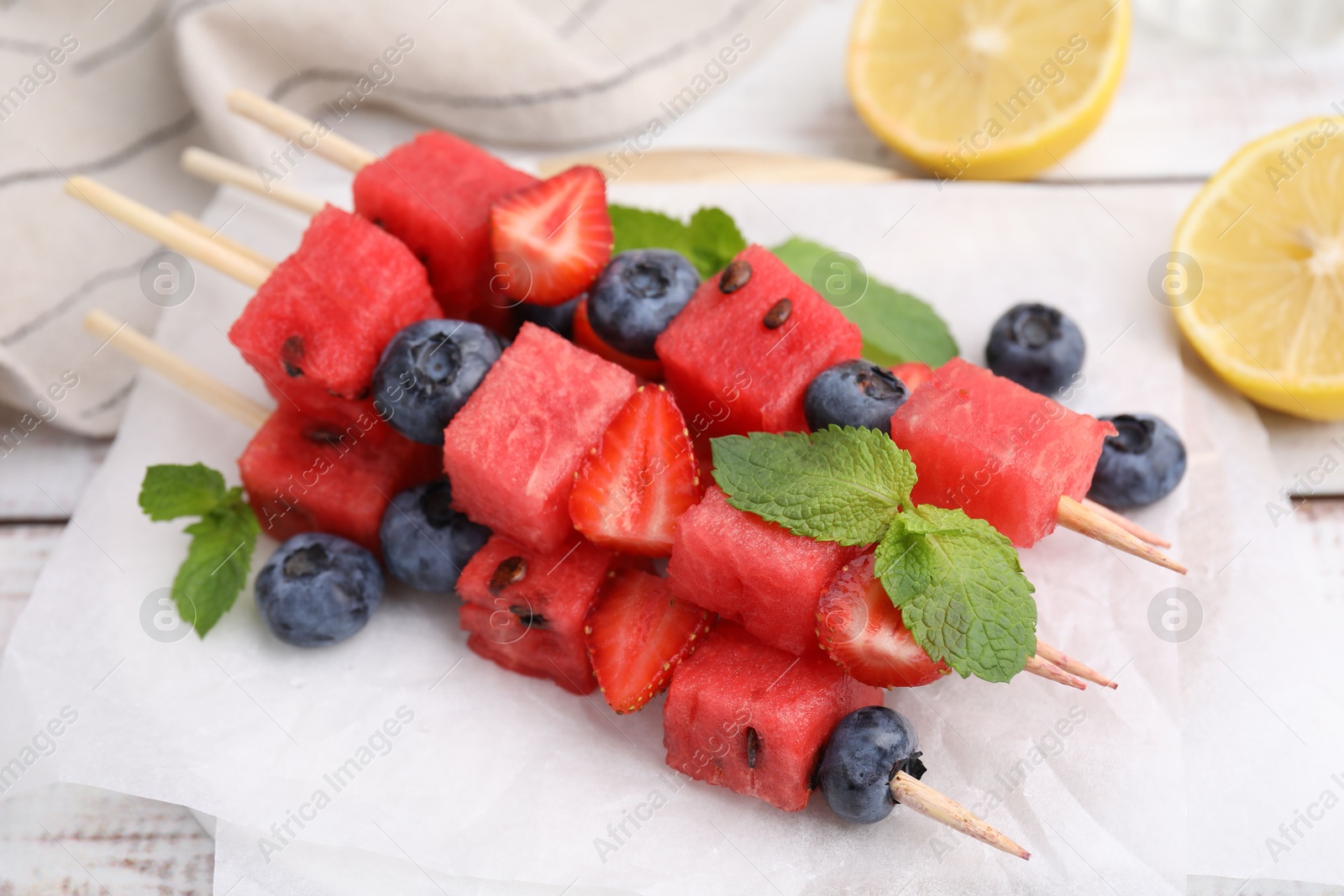 Photo of Skewers with tasty watermelon, strawberries, blueberries and mint on table, closeup