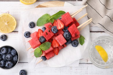 Photo of Skewers with tasty watermelon, strawberries, blueberries and mint on light wooden table, flat lay