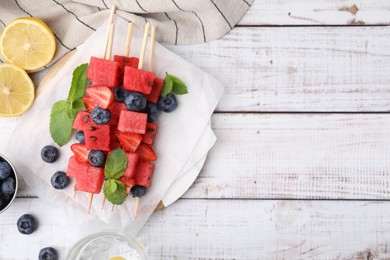 Photo of Skewers with tasty watermelon, strawberries, blueberries and mint on light wooden table, flat lay. Space for text