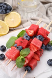 Skewers with tasty watermelon, strawberries, blueberries and mint on table, closeup