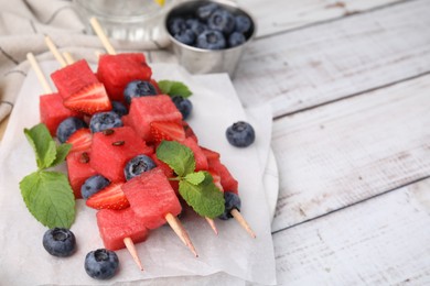 Photo of Skewers with tasty watermelon, strawberries, blueberries and mint on light wooden table, closeup. Space for text