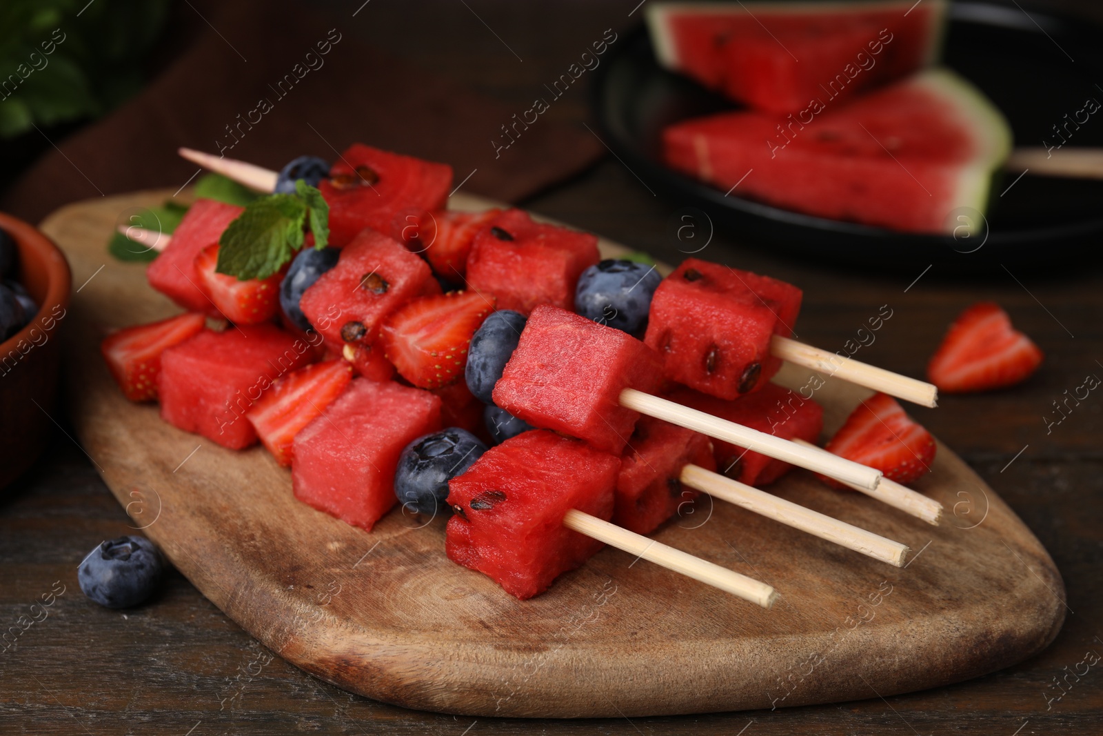 Photo of Skewers with tasty watermelon, strawberries, blueberries and mint on wooden table, closeup