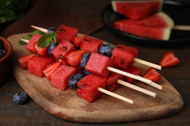 Photo of Skewers with tasty watermelon, strawberries, blueberries and mint on wooden table, closeup