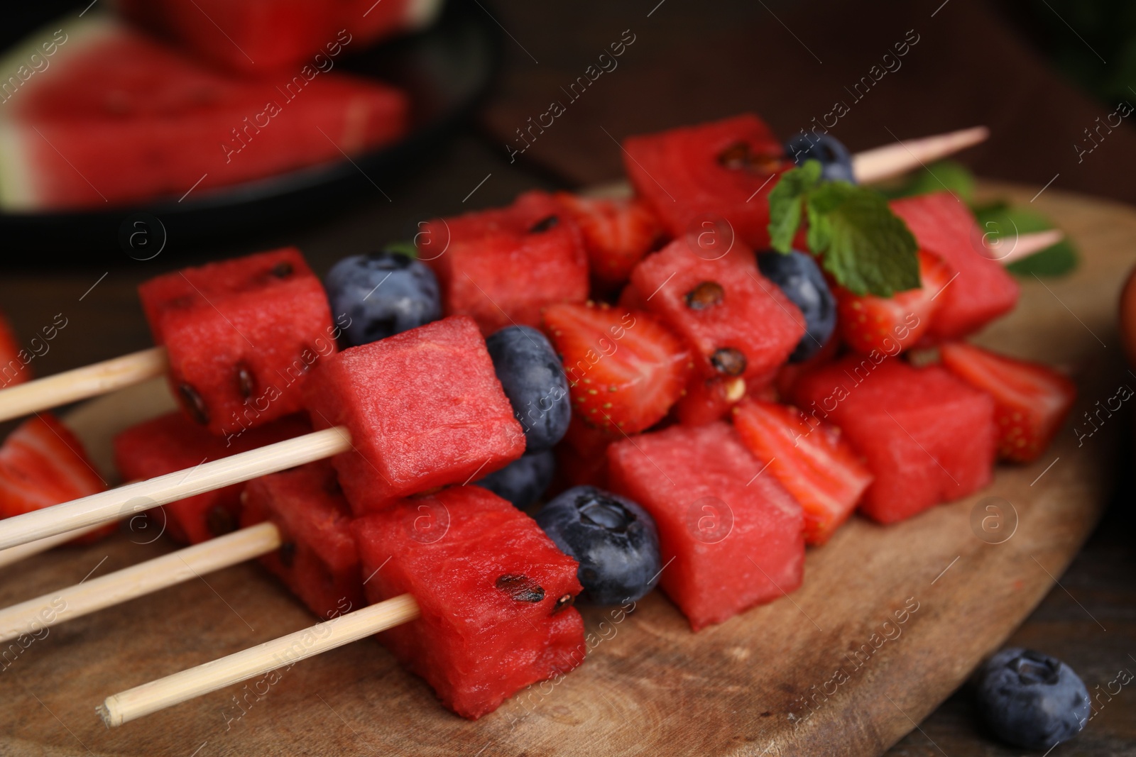 Photo of Skewers with tasty watermelon, strawberries, blueberries and mint on table, closeup