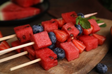 Photo of Skewers with tasty watermelon, strawberries, blueberries and mint on table, closeup