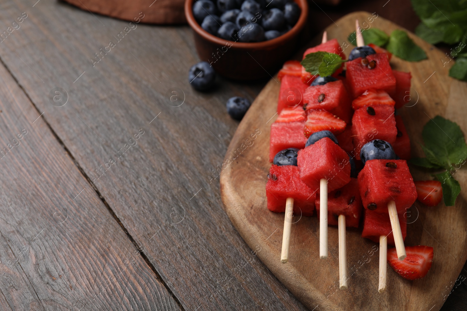 Photo of Skewers with tasty watermelon, strawberries, blueberries and mint on wooden table, closeup. Space for text