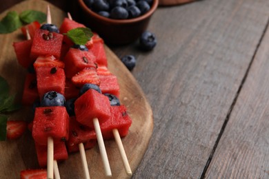 Photo of Skewers with tasty watermelon, strawberries, blueberries and mint on wooden table, closeup. Space for text