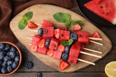 Photo of Skewers with tasty watermelon, strawberries, blueberries and mint on wooden table, flat lay