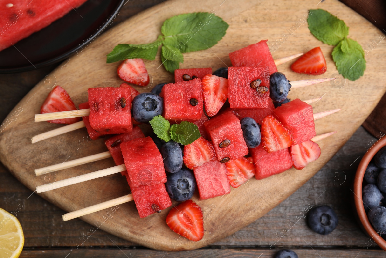 Photo of Skewers with tasty watermelon, strawberries, blueberries and mint on wooden table, flat lay