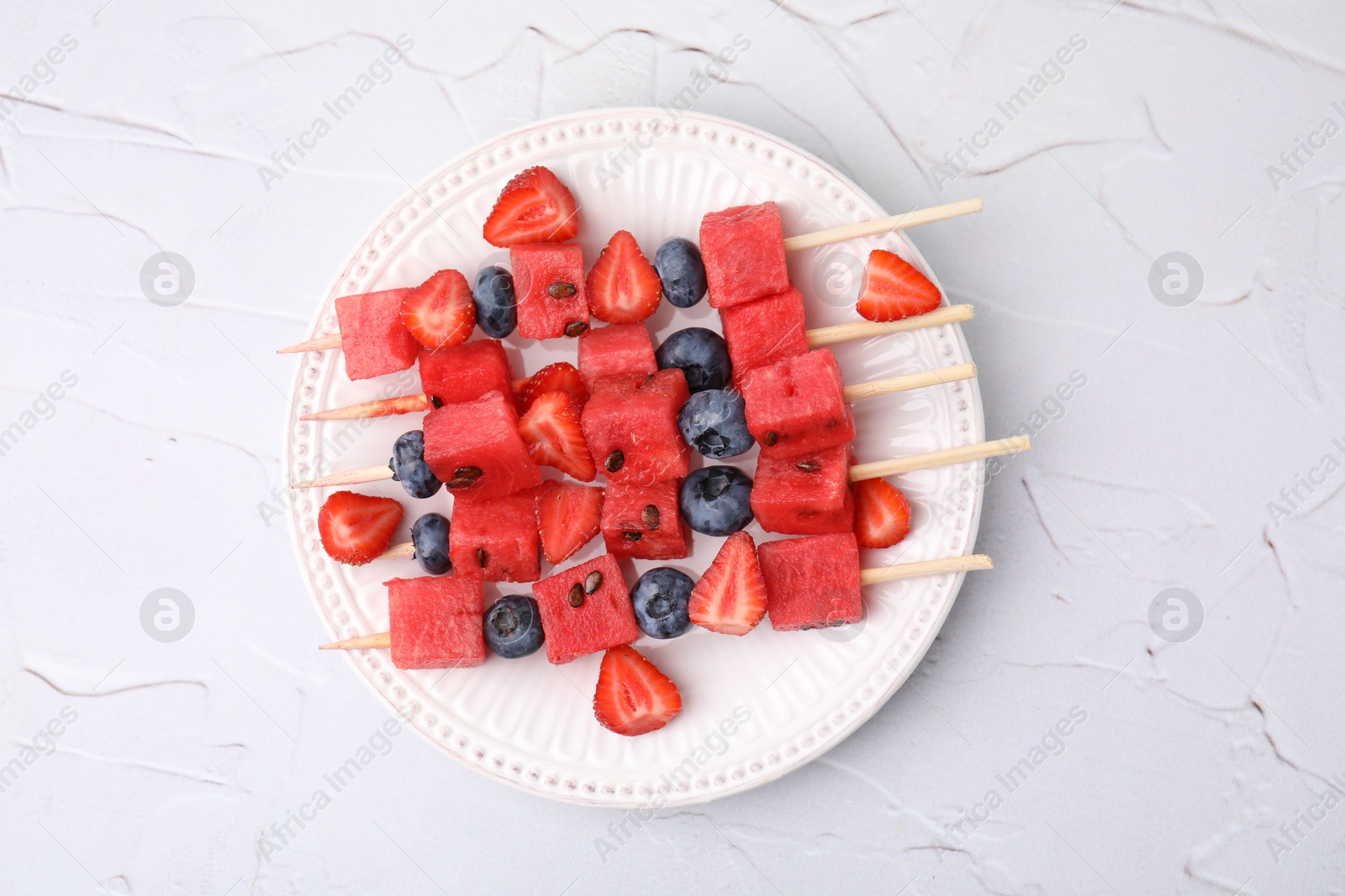 Photo of Skewers with tasty watermelon, strawberries and blueberries on white textured table, top view