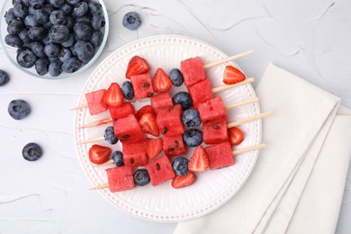 Photo of Skewers with tasty watermelon, strawberries and blueberries on white textured table, flat lay