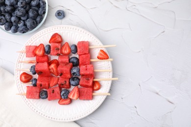 Photo of Skewers with tasty watermelon, strawberries and blueberries on white textured table, flat lay. Space for text