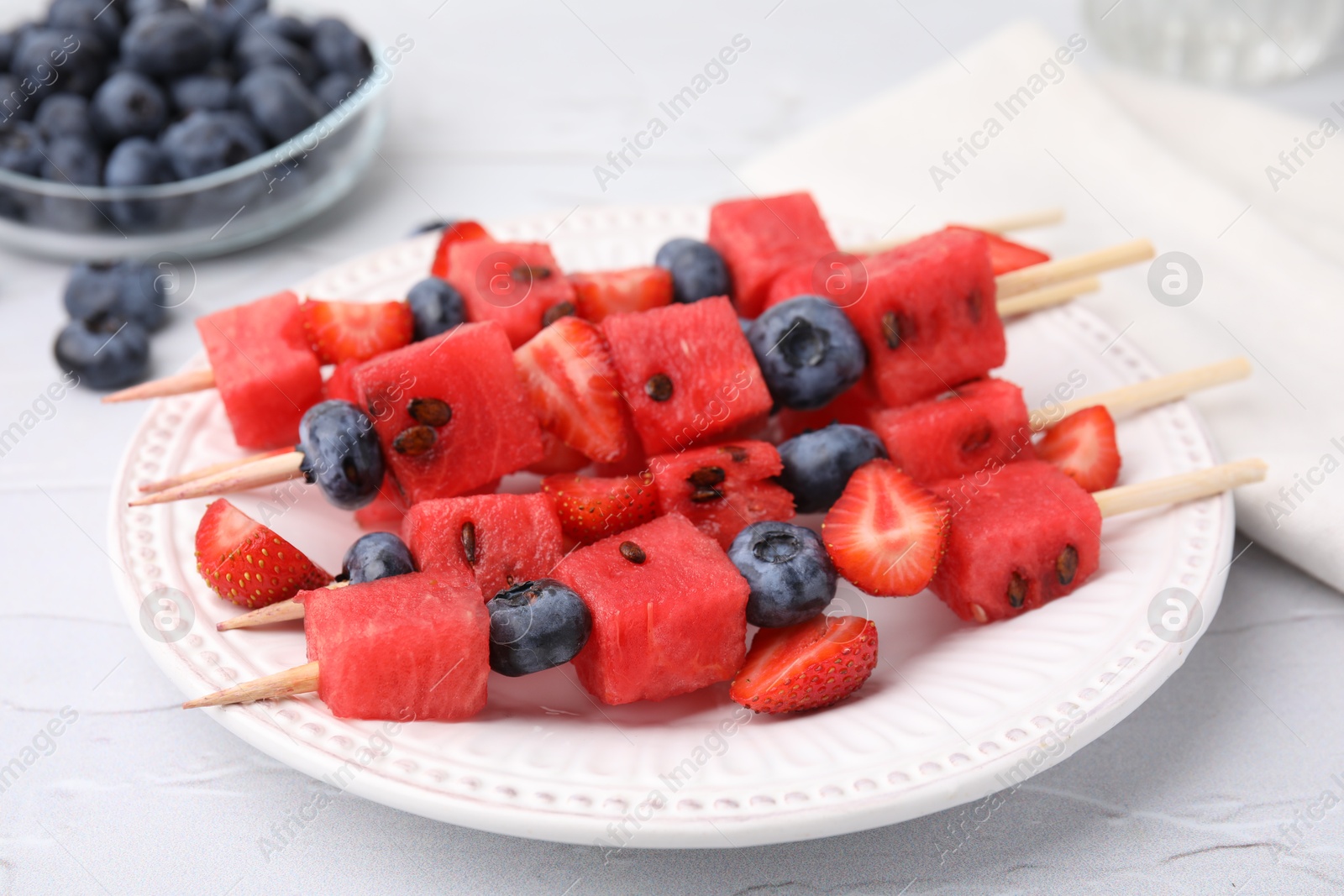 Photo of Skewers with tasty watermelon, strawberries and blueberries on white table, closeup