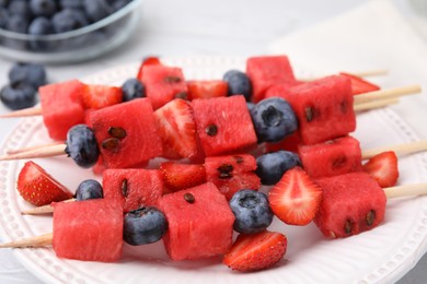 Photo of Skewers with tasty watermelon, strawberries and blueberries on white plate, closeup