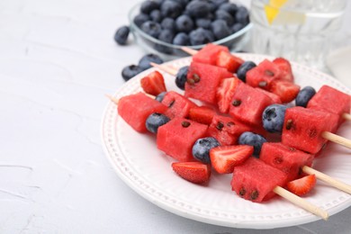 Photo of Skewers with tasty watermelon, strawberries and blueberries on white table, closeup