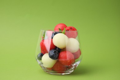 Photo of Tasty watermelon and melon balls with blueberries in glass on green table