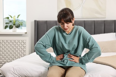 Upset woman suffering from abdominal pain on bed at home