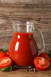 Tasty tomato juice in glass jug, fresh vegetables and spices on wooden table