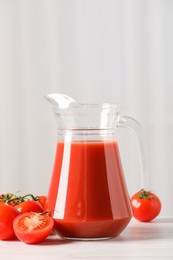 Photo of Tasty tomato juice in glass jug and fresh vegetables on white table