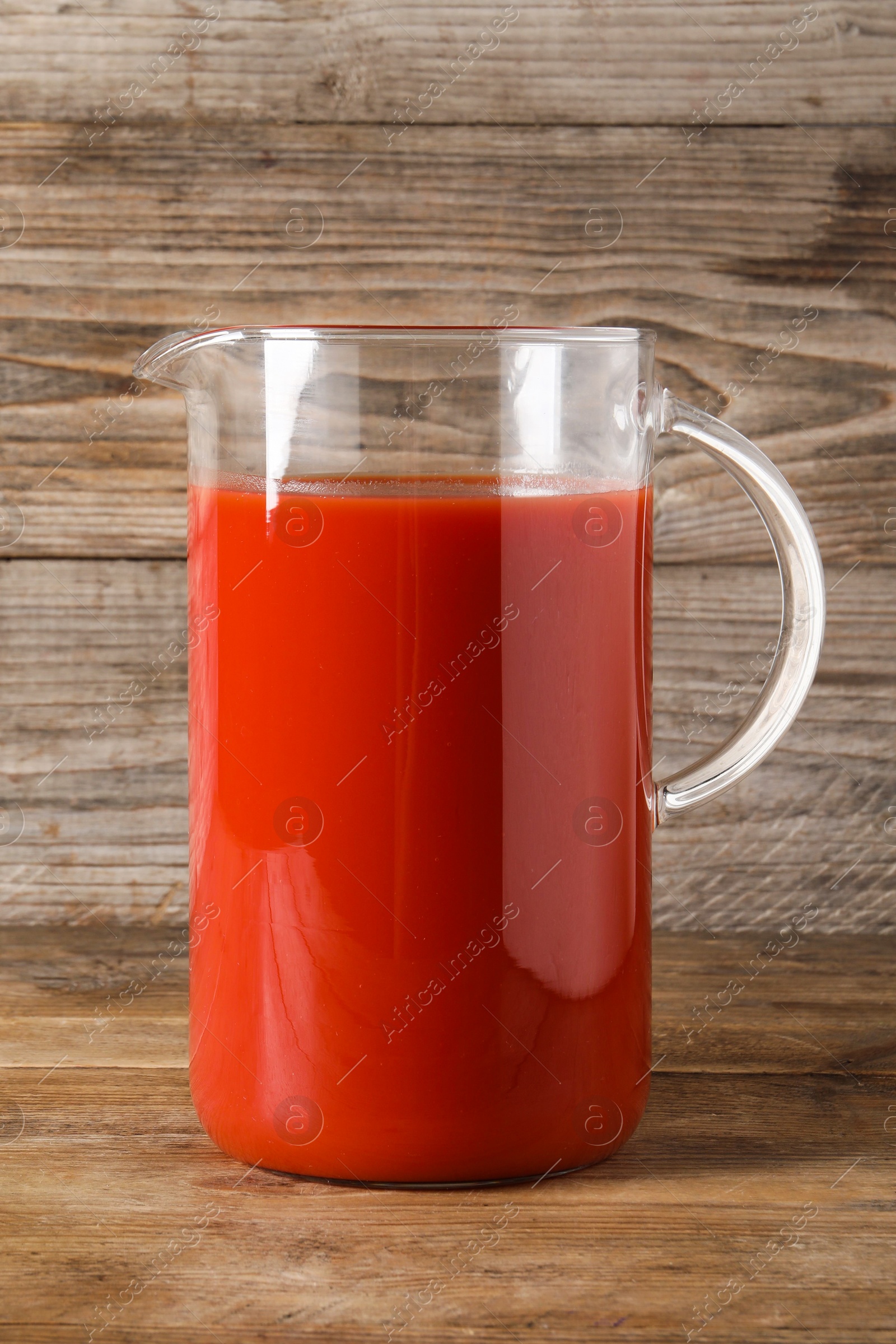 Photo of Fresh tomato juice in glass jug on wooden table