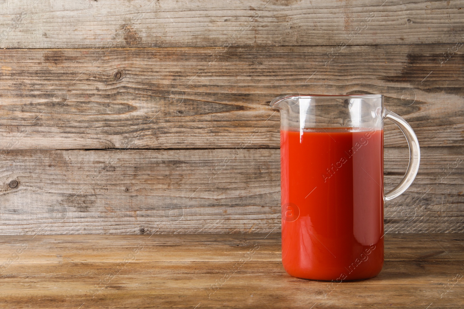 Photo of Fresh tomato juice in glass jug on wooden table, space for text