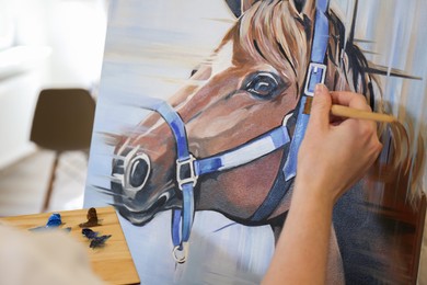 Photo of Woman drawing cute horse with brush in studio, closeup