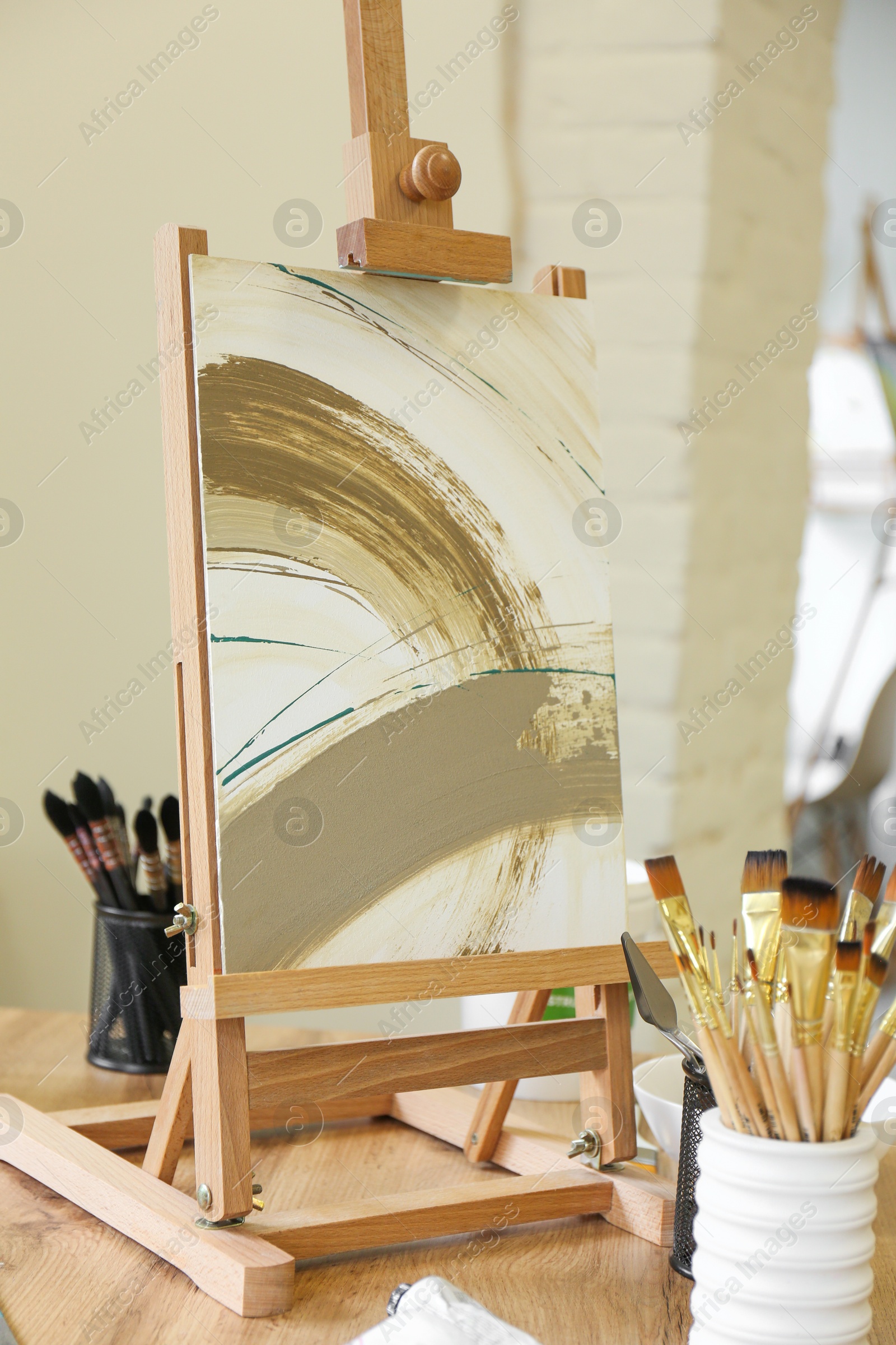 Photo of Small easel with abstract picture and art supplies on table in drawing studio