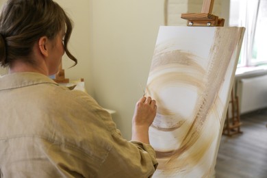 Photo of Woman drawing on easel with canvas in studio