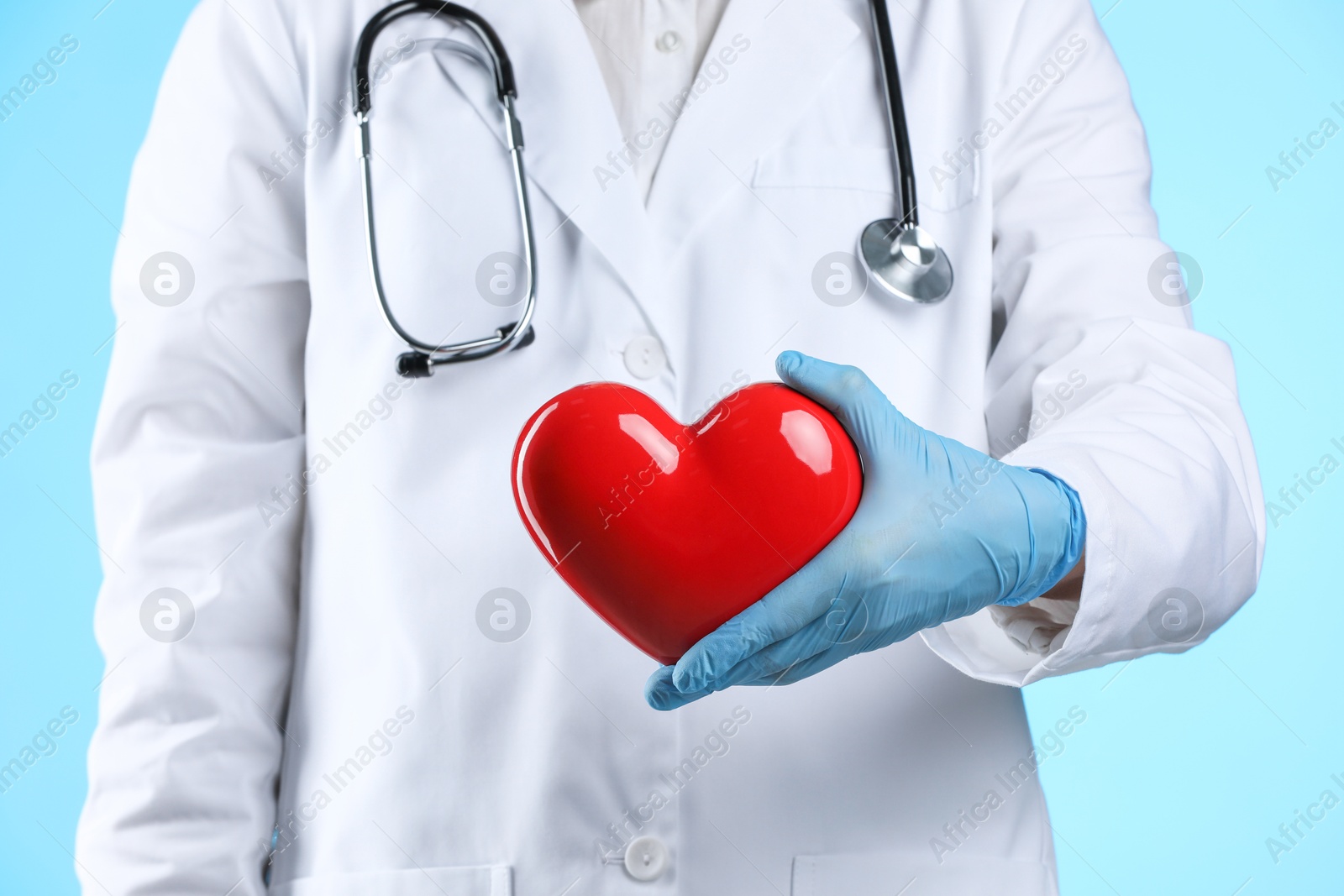 Photo of Doctor with red heart on light blue background, closeup