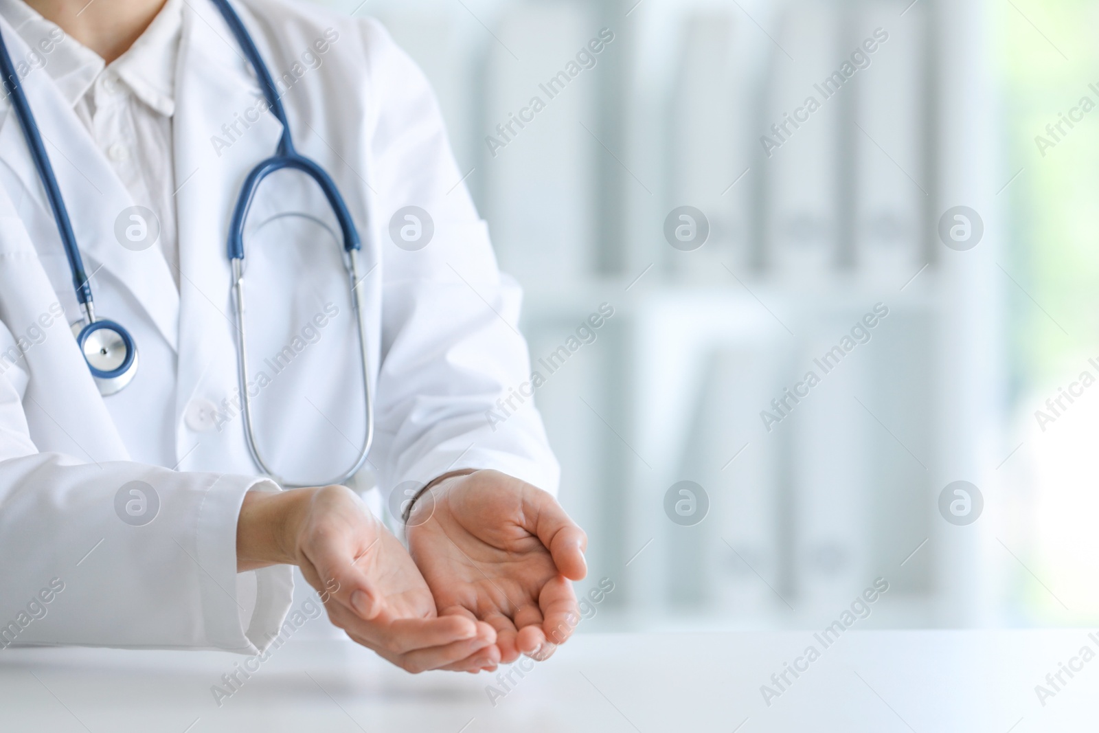 Photo of Doctor with stethoscope holding something at table in clinic, closeup. Space for text