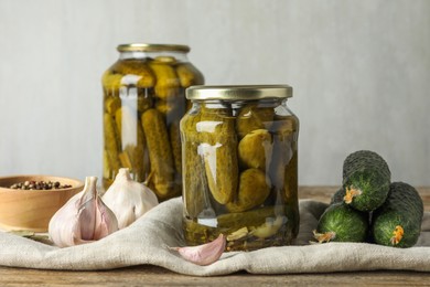 Pickles in jars, fresh cucumbers and spices on wooden table