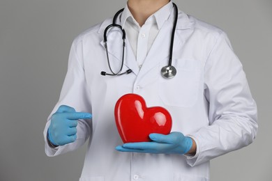 Doctor with red heart on grey background, closeup