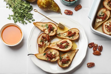 Photo of Delicious baked pears with nuts, blue cheese, thyme and honey on white tiled table, flat lay