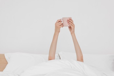 Photo of Bedtime. Woman with cup of drink in bed indoors, closeup