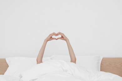 Photo of Bedtime. Woman showing heart gesture with hands in bed indoors, closeup