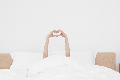 Bedtime. Woman showing heart gesture with hands in bed indoors, closeup