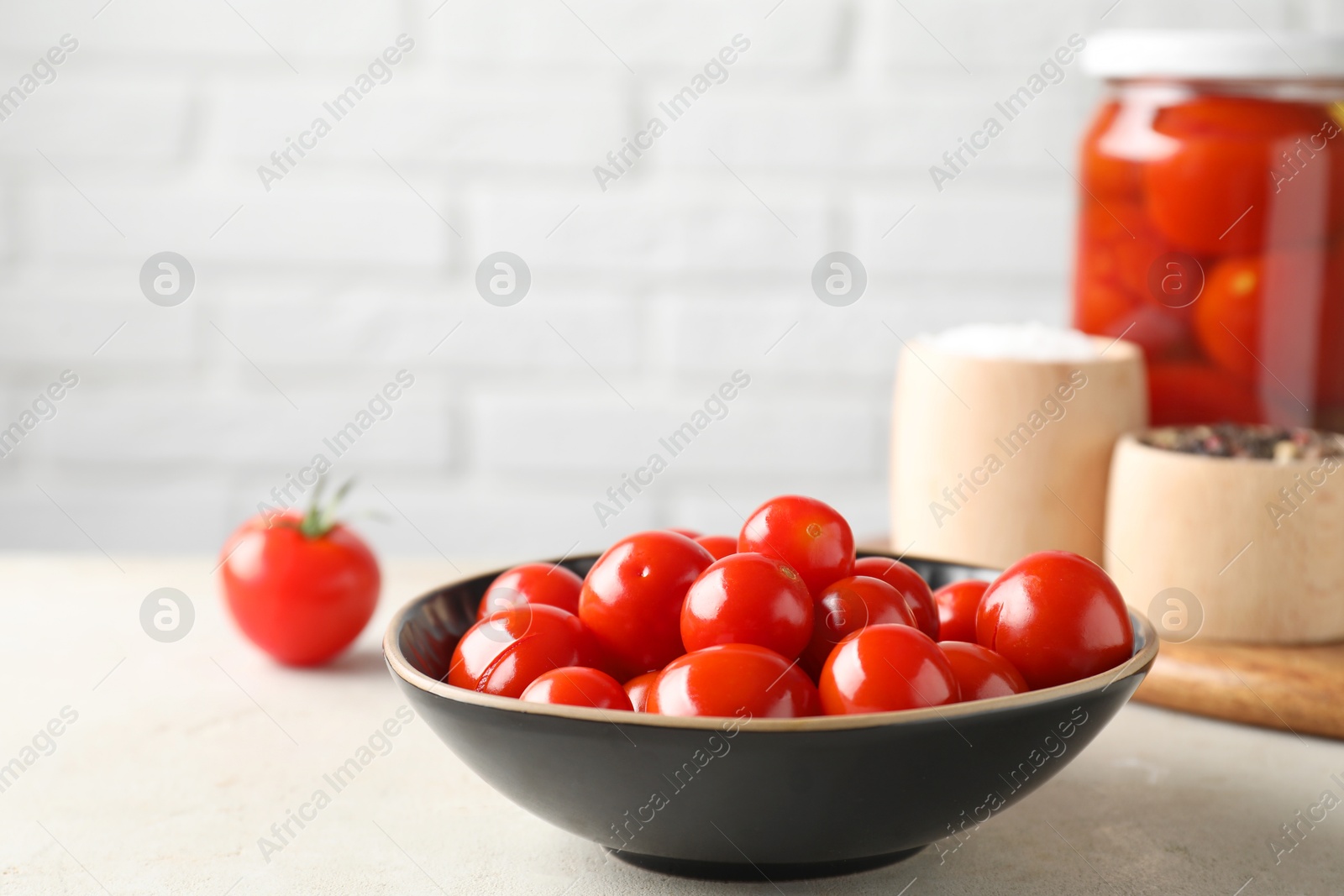 Photo of Tasty pickled tomatoes in bowl and spices on light grey table