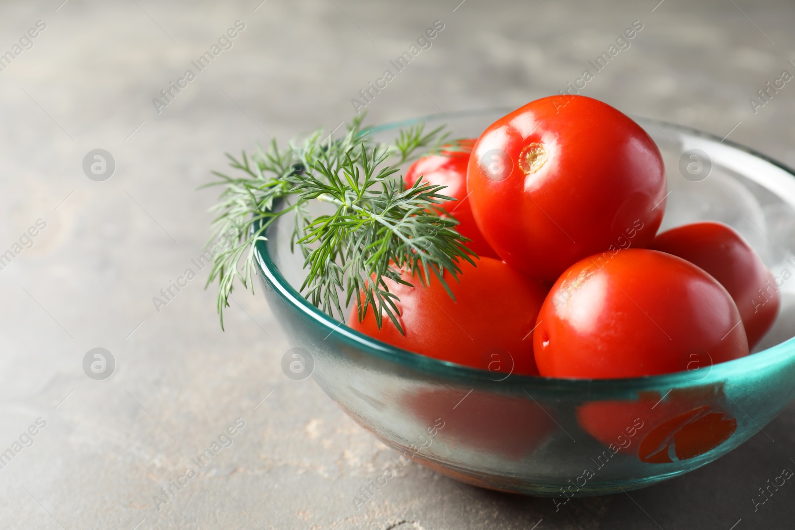 Photo of Tasty pickled tomatoes and dill in bowl on grey table, closeup