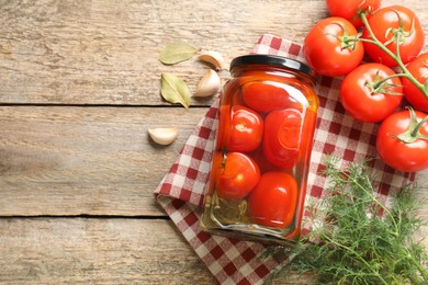 Tasty pickled tomatoes in jar, spices and fresh vegetables on wooden table, top view. Space for text