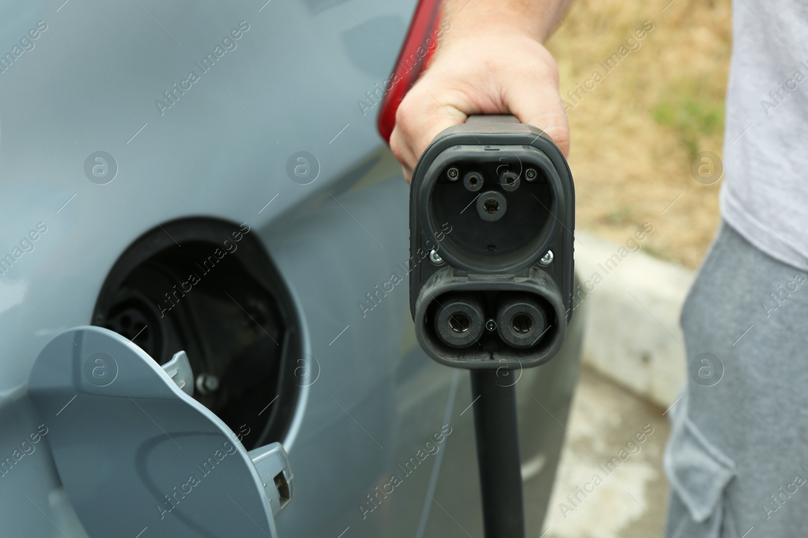 Photo of Man inserting plug into electric car socket at charging station outdoors, closeup