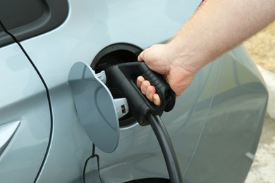 Photo of Man inserting plug into electric car socket at charging station outdoors, closeup