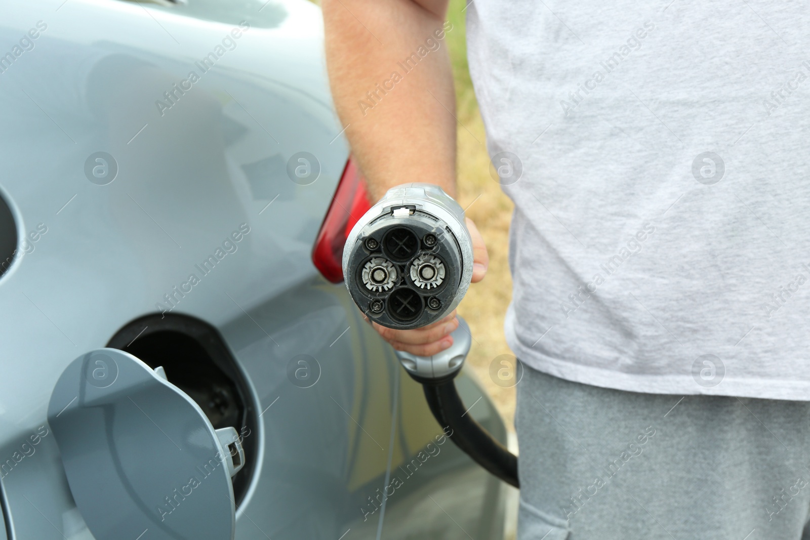 Photo of Man inserting plug into electric car socket at charging station outdoors, closeup