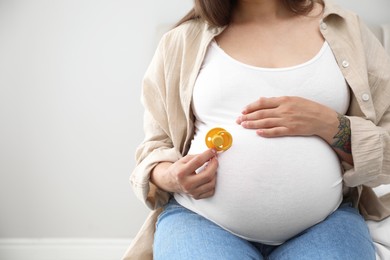 Photo of Pregnant woman with yellow pacifier on light background, closeup. Space for text