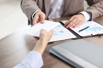 Photo of Boss giving salary in paper envelope to employee indoors, closeup